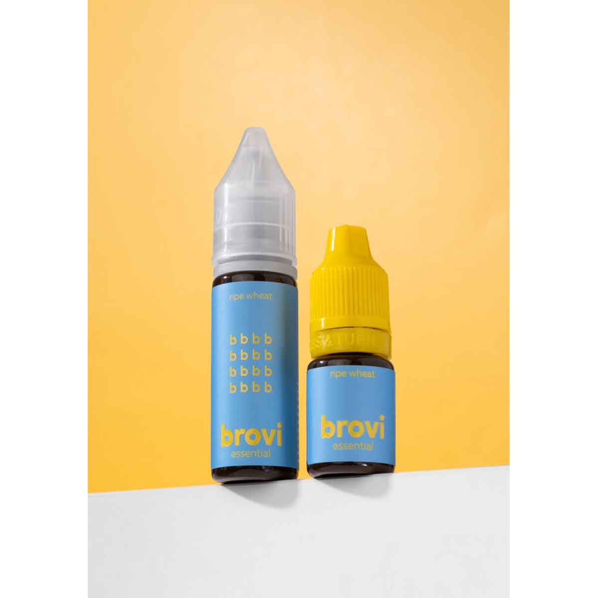 Two Brovi e-liquid bottles standing on a white surface against a yellow background. One bottle has a clear cap and a light blue label with gold text, and the other has a yellow cap and a matching light blue label.
