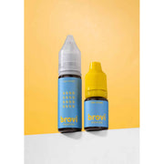 Two Brovi e-liquid bottles standing on a white surface against a yellow background. One bottle has a clear cap and a light blue label with gold text, and the other has a yellow cap and a matching light blue label.
