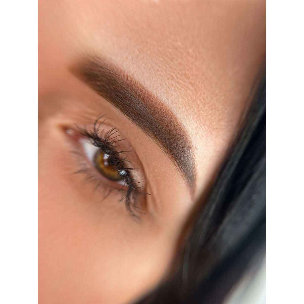 Close-up of a woman's eye and eyebrow with a filled, dark brown eyebrow and long eyelashes.