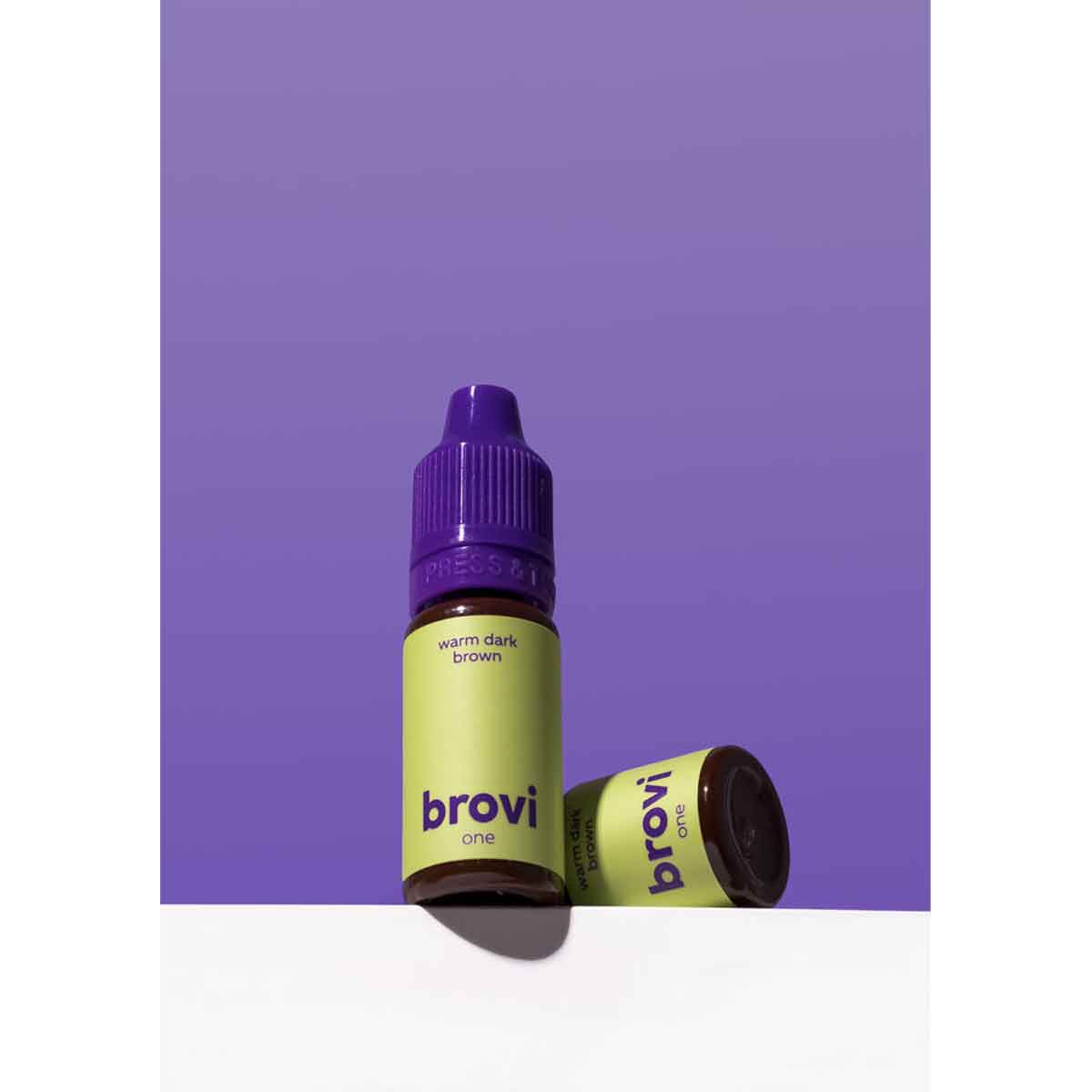A bottle of Brovi One e-liquid in the 'warm dark brown' flavor, standing upright next to its cap on a white surface against a solid purple background.