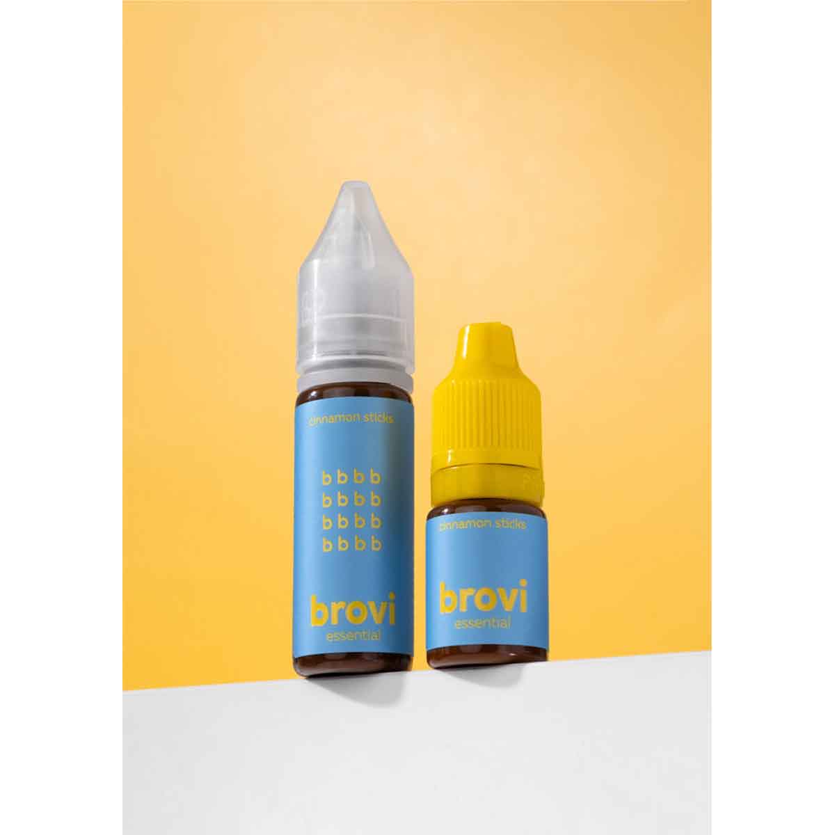 Two Brovi e-liquid bottles in the cinnamon sugar flavor, one with a clear cap and one with a yellow cap, standing on a white surface against a yellow background.