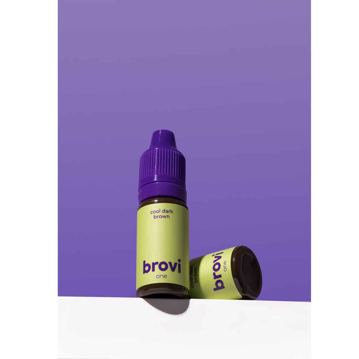 Two Brovi One e-liquid bottles in 'cool dark brown' flavor, featuring lime green labels and purple caps, set against a solid purple background with one bottle lying on its side.