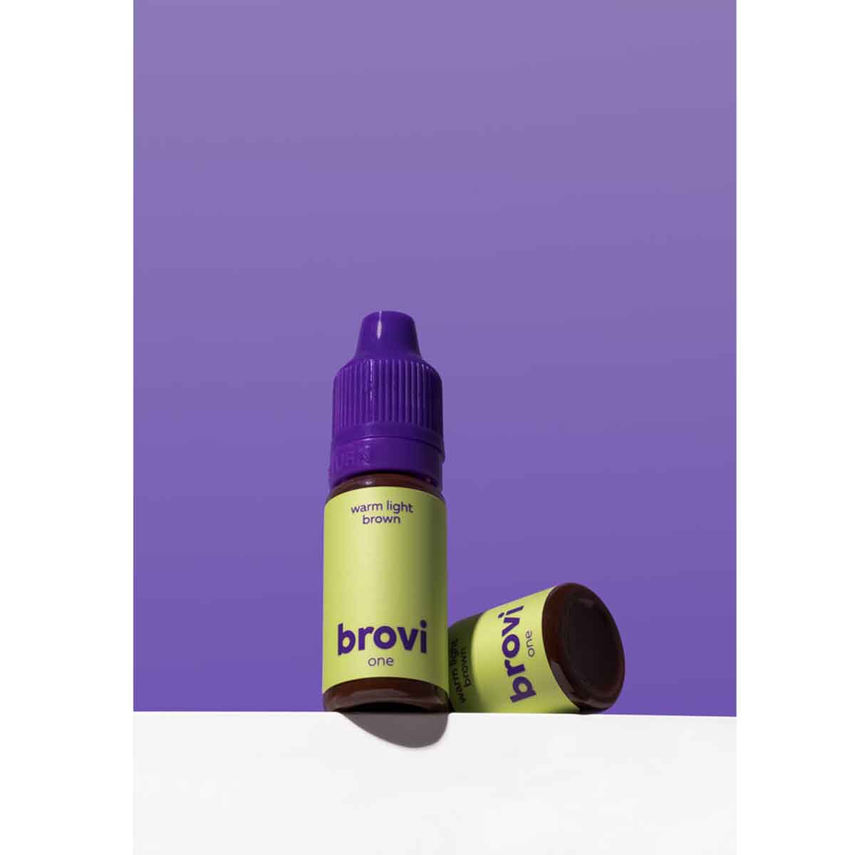 A bottle of Brovi One e-liquid in the 'warm light brown' flavor, standing upright with its cap removed and lying on its side. The bottle features a lime green label with dark purple text, and the cap is a deep purple.