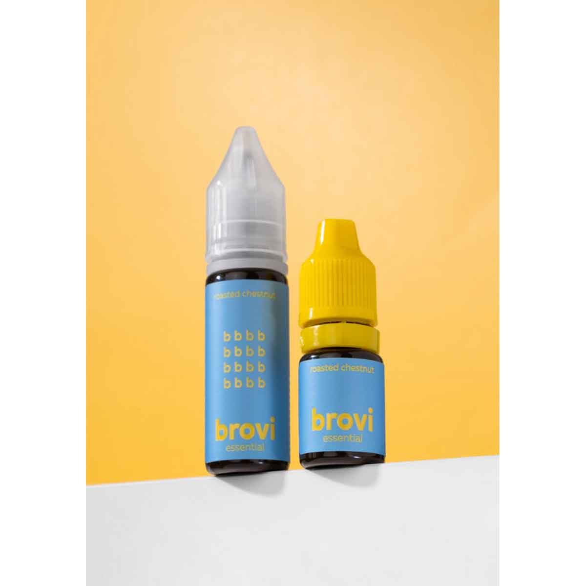 Two small Brovi essential oil bottles standing on a white surface against a yellow background. The taller bottle has a clear cap and a light blue label, while the shorter bottle has a bright yellow cap and a matching light blue label.