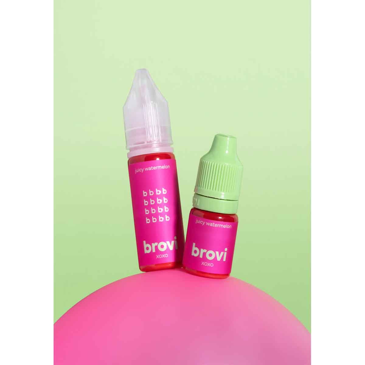 Two Brovi e-liquid bottles, one with a pink cap and one with a light green cap, standing on a pink sphere against a light green background.