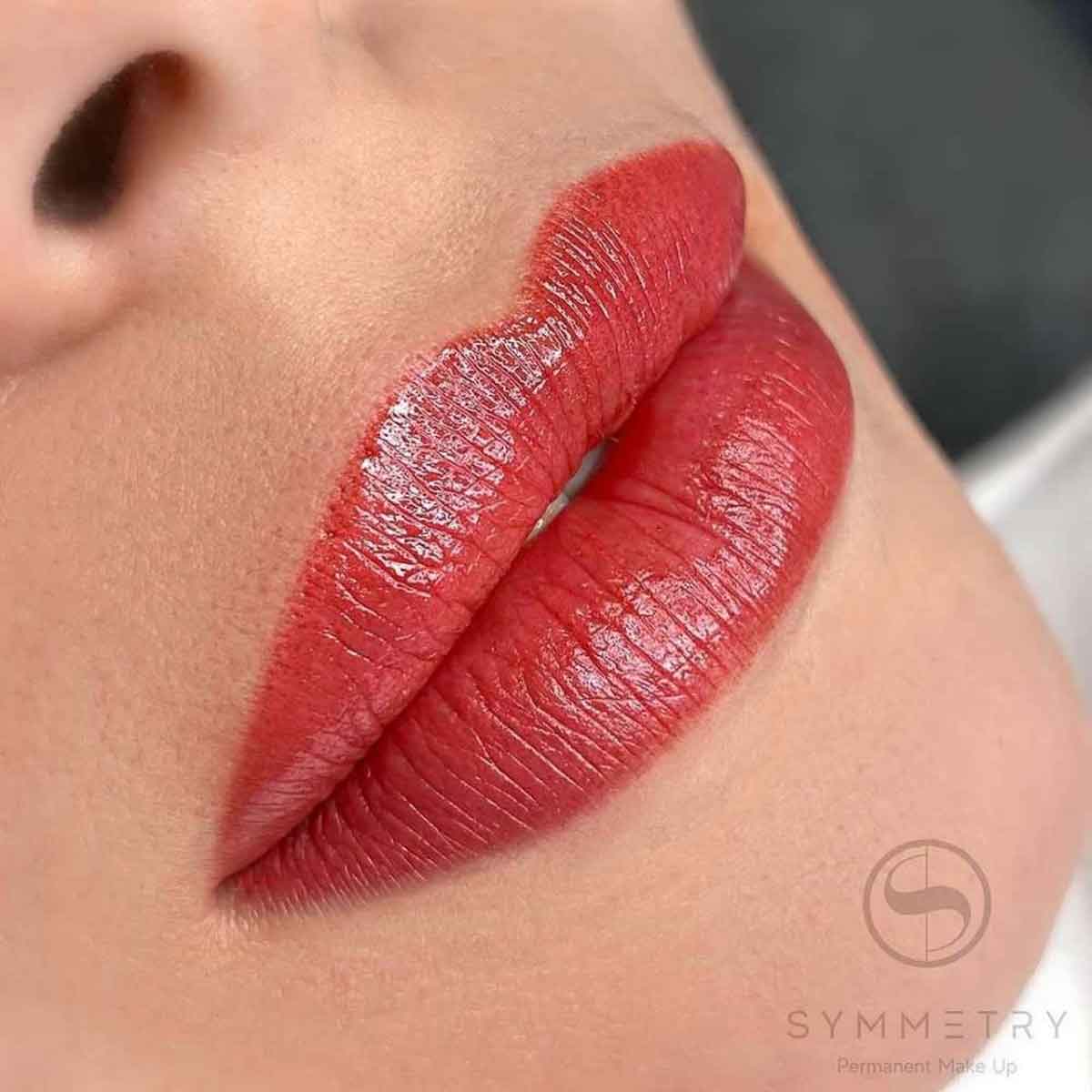 Close-up of a person's lips showcasing a glossy, long-lasting red lipstick or lip tint. The brand name 'SYMMETRY' with the tagline 'Permanent Make Up' is visible as a watermark in the bottom right corner.