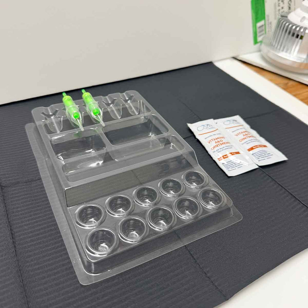 Clear plastic tattoo work tray with compartments on a dark surface