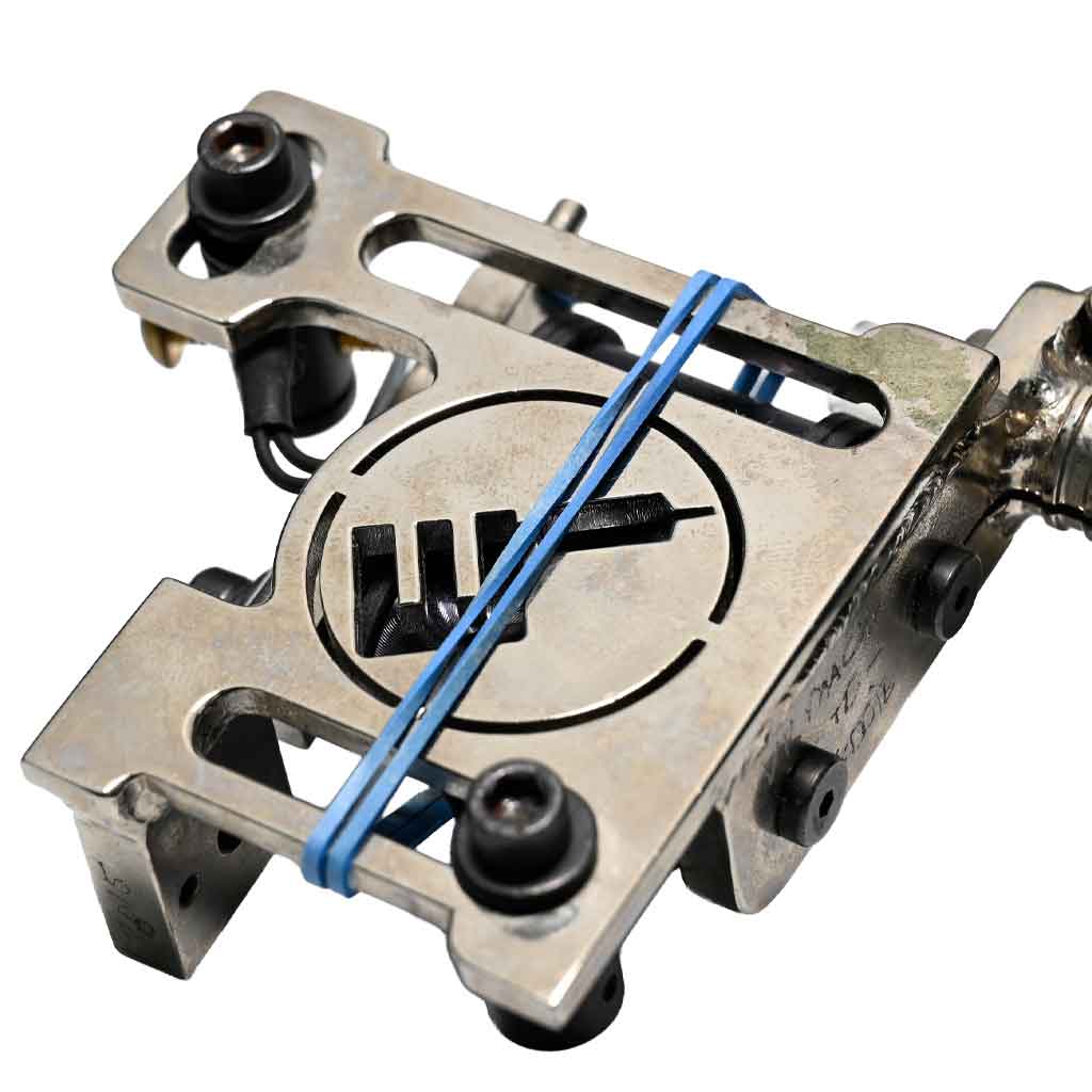 Side view of a chrome tattoo coil machine featuring a blue rubber band for needle stabilization.