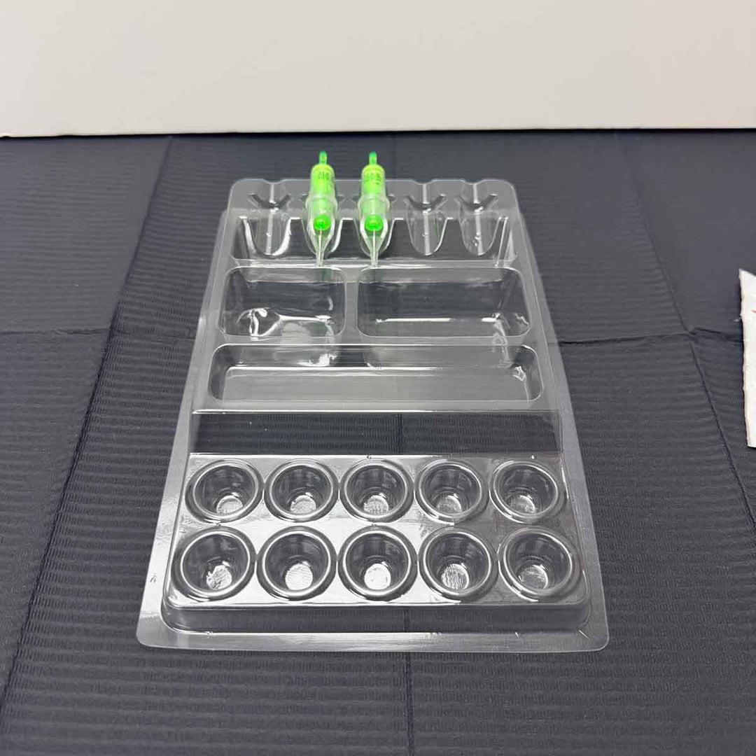 Clear plastic tattoo work tray with multiple compartments on a textured surface