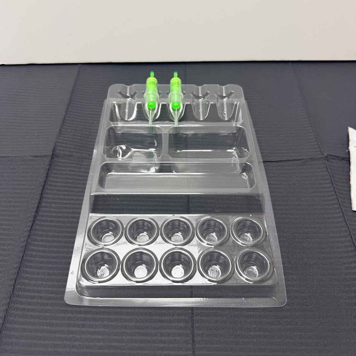 Clear plastic tattoo work tray with multiple compartments on a textured surface